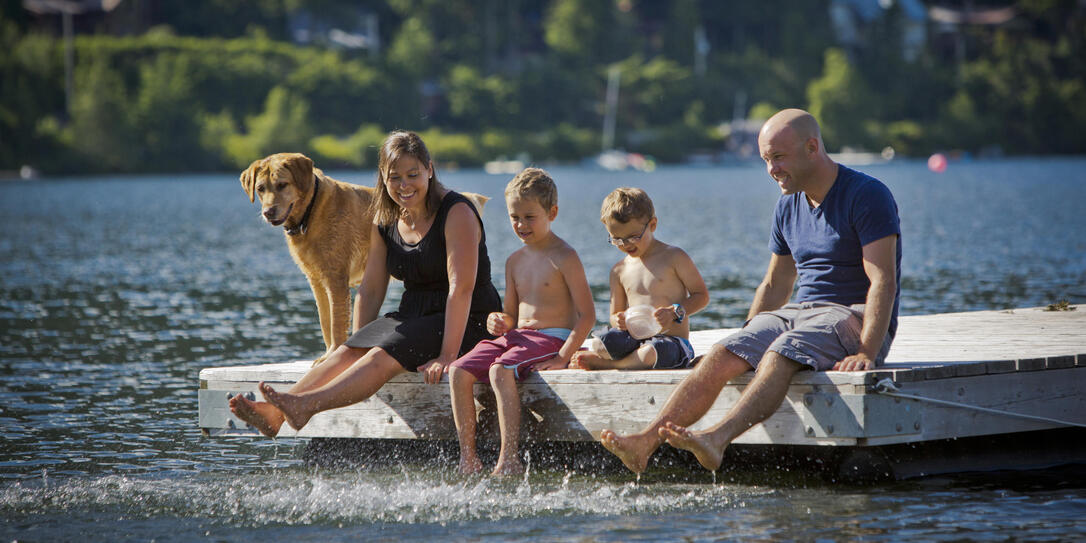 Young family with pet sitting on dock by lake.