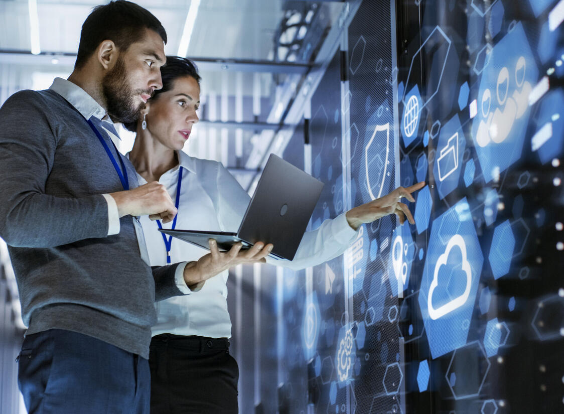 Male IT Specialist Holds Laptop and Discusses Work with Female Server Technician. They're Standing in Data Center, Rack Server Cabinet with Cloud Server Icon and Visualization. Male IT Specialist Holds Laptop and Discusses Work with Female Server Technician. They're Standing in Data Center, Rack Server Cabinet with Cloud Server Icon and Visualization.
