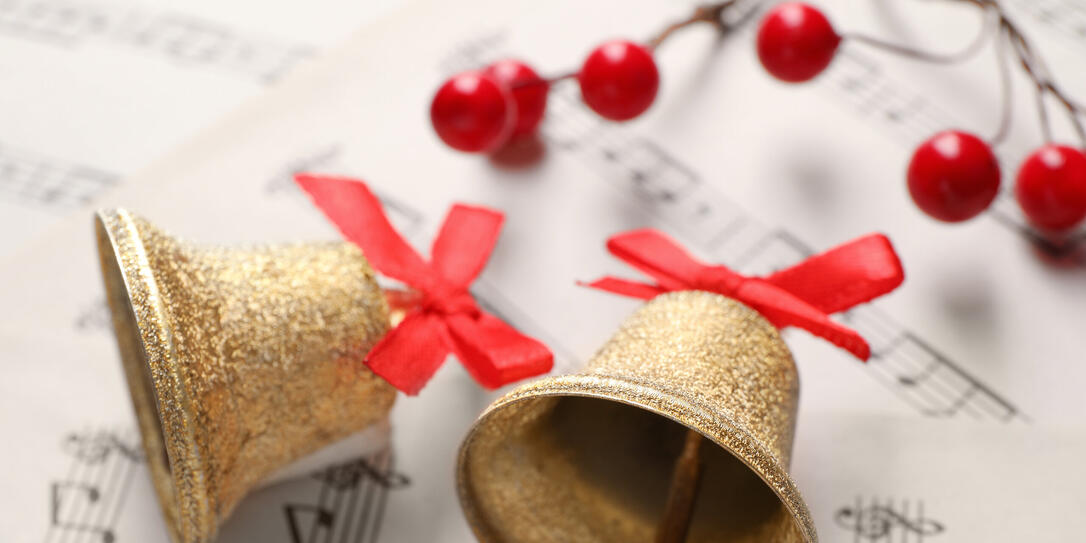 Golden shiny bells with red bows and decorative berries on music sheets, closeup. Christmas decoration