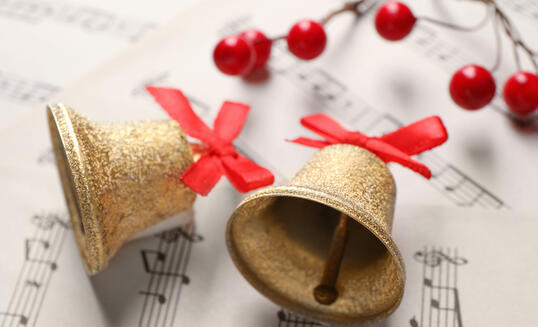 Golden shiny bells with red bows and decorative berries on music sheets, closeup. Christmas decoration