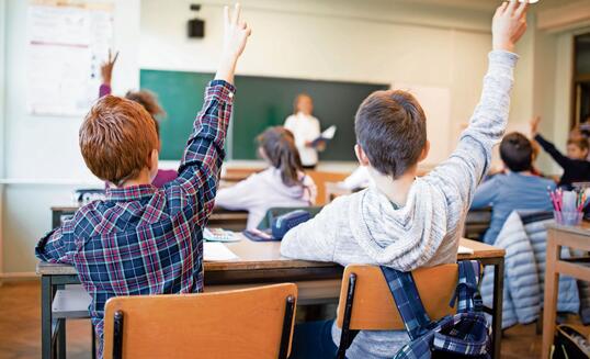 Schoolchildren at classroom with raised hands answering teacher's question.