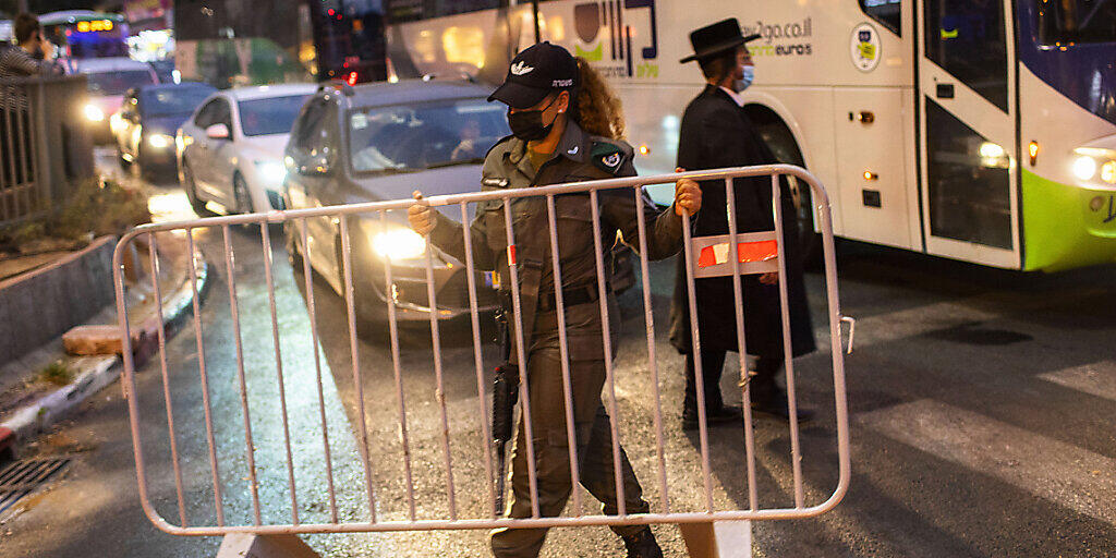 dpatopbilder - Ein israelischer Grenzpolizist errichtet in der ultra-orthodoxen jüdischen Stadt Bnei Brak vor einer nächtlichen Ausgangssperre auf einer Hauptstraße eine Absperrung. Foto: Oded Balilty/AP/dpa