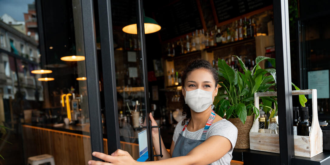 Happy business owner opening the door at a cafe wearing a facemask