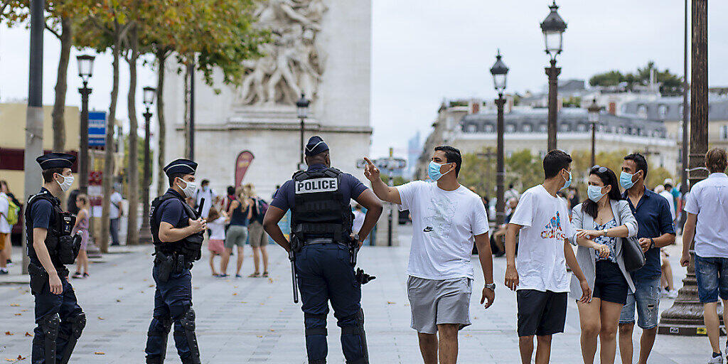 dpatopbilder - Touristen mit Schutzmasken gehen auf der Prachtstraße Champs-Elysees an Polizisten vorbei. Foto: Kamil Zihnioglu/AP/dpa