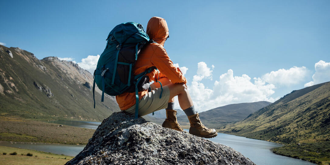 Backpacking woman sit on high altitude mountain top,enjoy the view of a lake in the distance Backpacking woman sit on high altitude mountain top,enjoy the view of a lake in the distance