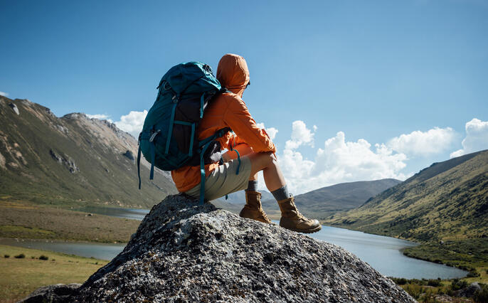 Backpacking woman sit on high altitude mountain top,enjoy the view of a lake in the distance