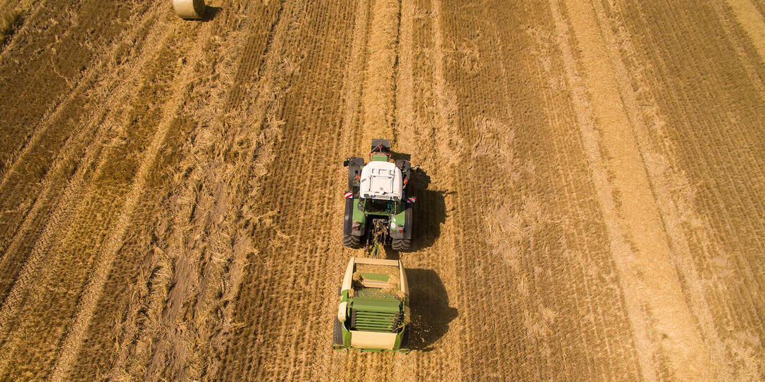 Aerial view of tractor with trailer at working in the golden wheat field - trailer makes straw bales - harvest in the summer - top view - Germany