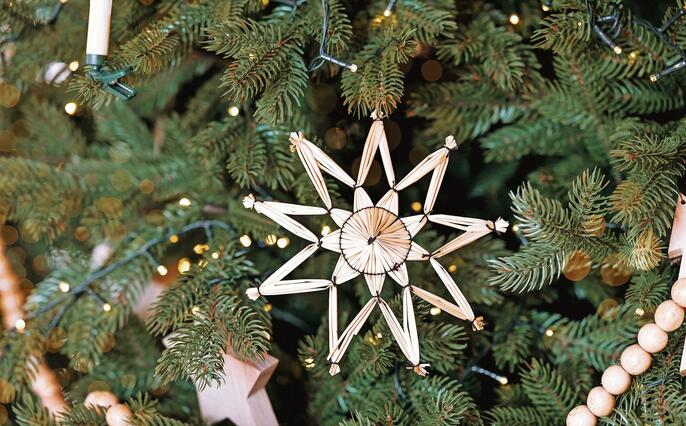 Decorative straw star ornament on a green Christmas tree adorned with lights