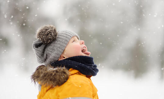 Cute little boy catching snowflakes with her tongue in beautiful winter park