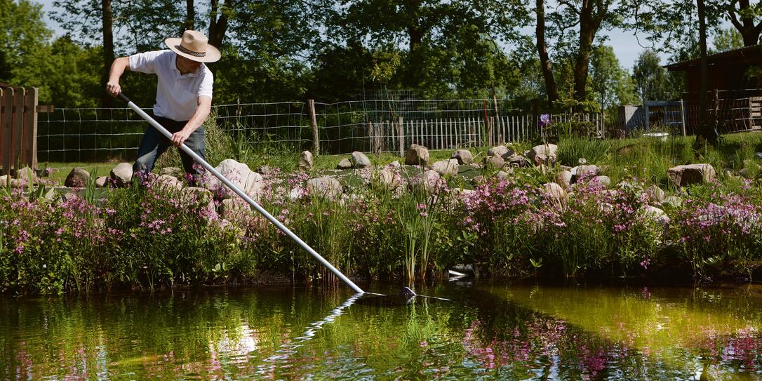 gardener with straw hat cleans pond