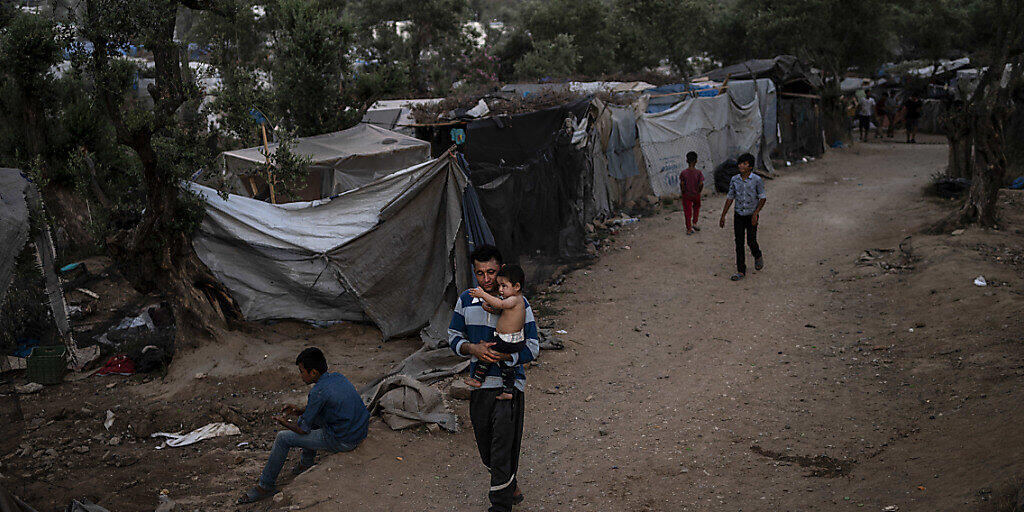 Ein Geflüchteter läuft mit einem Kind durch ein Übergangslager neben dem Flüchtlingslager Camp Moria. Foto: Angelos Tzortzinis/DPA