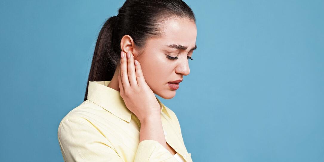 Young woman suffering from ear pain on light blue background. Space for text