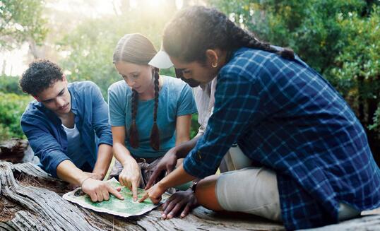 Map, nature and group of friends hiking in forest with route plan for adventure together. Travel, outdoor and people with paper guide for trekking in woods on weekend trip for discovery or journey.