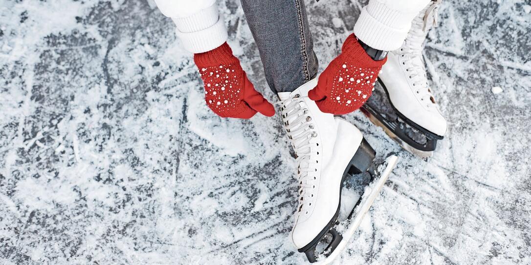 Girl tying shoelaces on ice skates before skating on the ice rink, hands in red knitted gloves.
