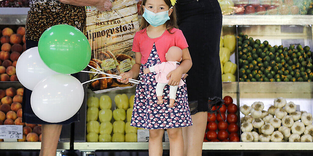 Ein Mädchen mit medizinischem Mundschutz hält Luftballons und eine Puppe in einem Lebensmittelmarkt in Bukarest. Rumänien verzeichnet einen Rekord an Neuinfektionen mit dem Coronavirus. Foto: Vadim Ghirda/AP/dpa Ein Mädchen mit medizinischem Mundschutz hält Luftballons und eine Puppe in einem Lebensmittelmarkt in Bukarest. Rumänien verzeichnet einen Rekord an Neuinfektionen mit dem Coronavirus. Foto: Vadim Ghirda/AP/dpa