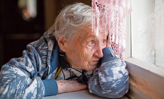 Elderly woman sadly looking out the window.