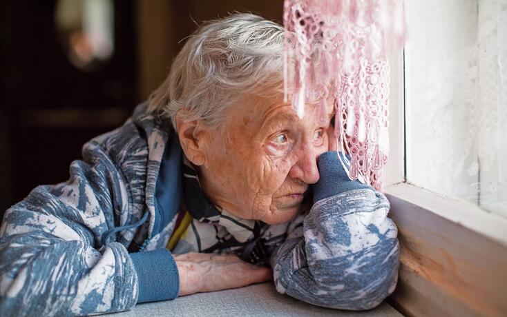 Elderly woman sadly looking out the window.