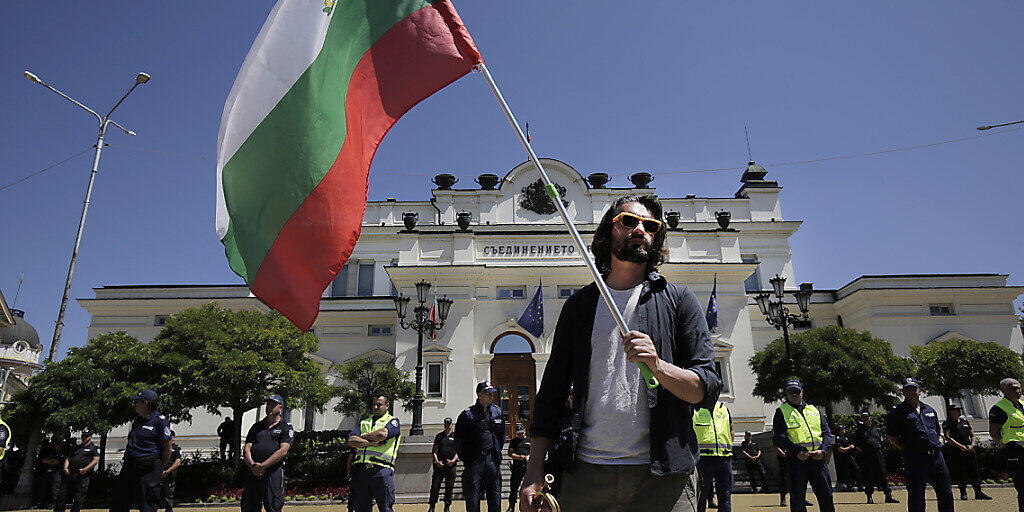 Ein Mann hält während einer Protestaktion vor dem bulgarischen Parlament die Fahne des Landes. Foto: Valentina Petrova/AP/dpa