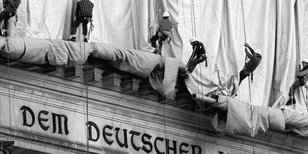 ARCHIV - Gewerbekletterer rollen die Verhüllungsplanen für den Berliner Reichstag vom Giebel des Bauwerks ab. Direkt über dem Haupteingang und der Schrift "Dem Deutschen Volke" fällt bei der Aktion des Verpackungskünstlers Christo der Stoff entlang der Säulen zu Boden. Foto: Wolfgang Kumm/dpa