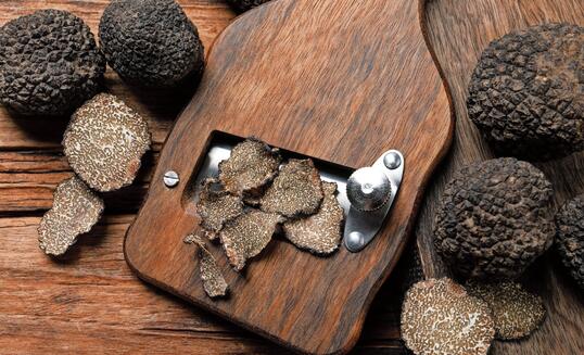 Shaver with whole and sliced black truffles on wooden table, flat lay