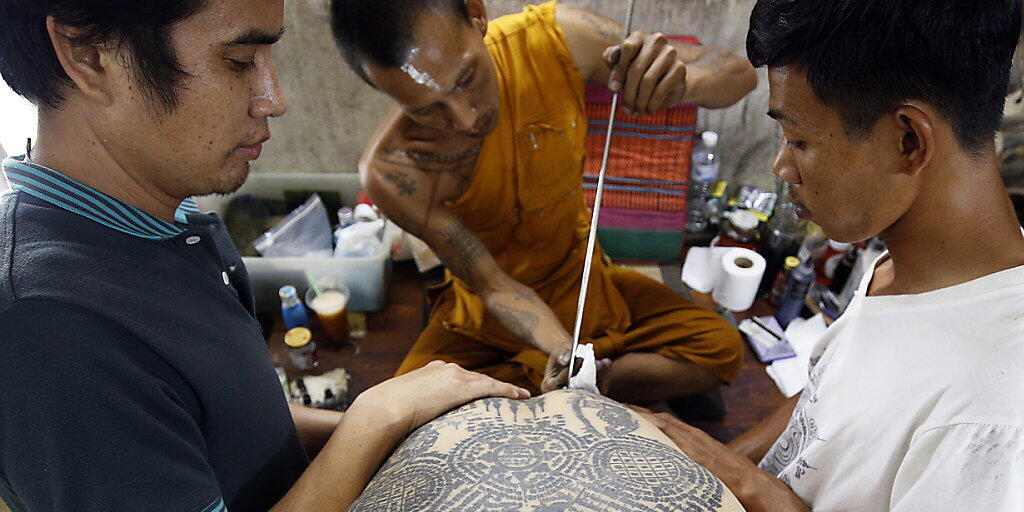 Auf dem traditionellen Tattoo-Fest im Wat-Bang-Phra-Tempel sticht ein buddhistischer Mönch einem Gläubigen mit einem angespitzten Stahlstab ein neues Tattoo.