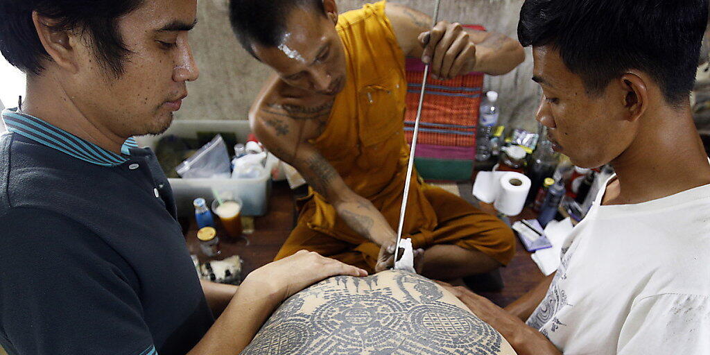 Auf dem traditionellen Tattoo-Fest im Wat-Bang-Phra-Tempel sticht ein buddhistischer Mönch einem Gläubigen mit einem angespitzten Stahlstab ein neues Tattoo. Auf dem traditionellen Tattoo-Fest im Wat-Bang-Phra-Tempel sticht ein buddhistischer Mönch einem Gläubigen mit einem angespitzten Stahlstab ein neues Tattoo.