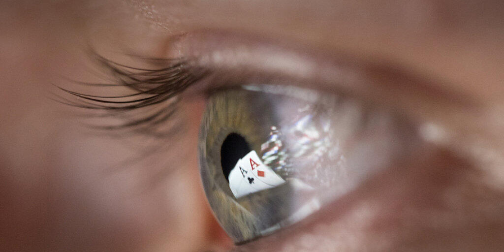 Zwei Ass-Spielkarten spiegeln sich in der Pupille eines Mannes, der Online-Poker spielt. Künftig dürfen auch Schweizer Casinos Online-Spiele anbieten.