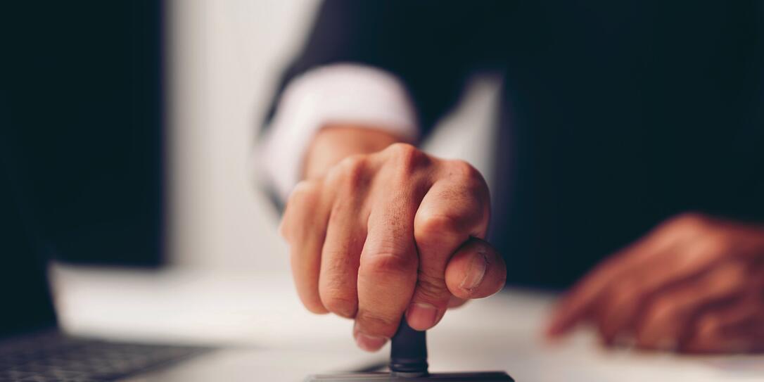 Close-up Of A Person's Hand Stamping With Approved Stamp On Document At Desk