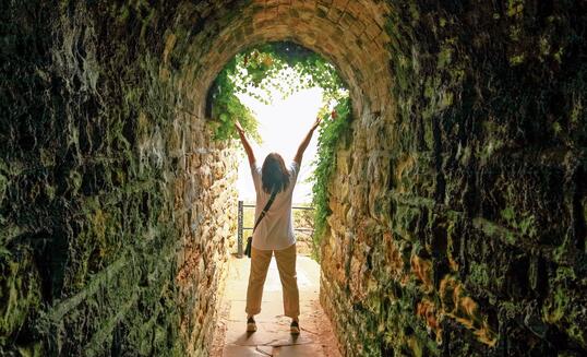 Silhouette of a lady with raised hands at the end of a tunnel