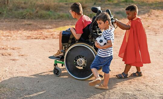 Diverse kids playing outdoors with wheelchair and soccer ball