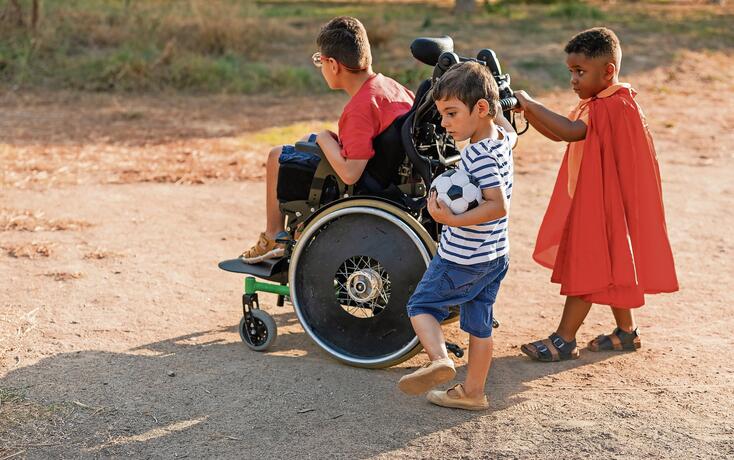 Diverse kids playing outdoors with wheelchair and soccer ball