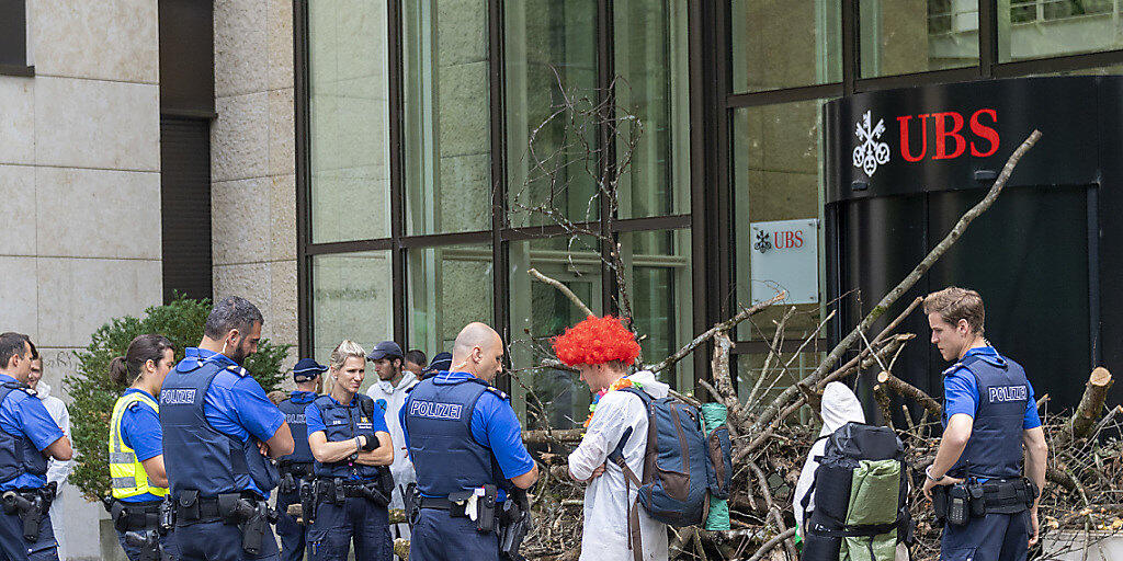 Polizisten räumten am Montag die Blockade der Aktivisten einer Gruppe namens "Collective Climate Justice" vor dem UBS-Bürogebäude am Aeschenplatz in Basel. Im Hintergrund eine Holzbeige, die an Schwemmholz erinnert, als Sperre vor der Türe. (Archivbild)